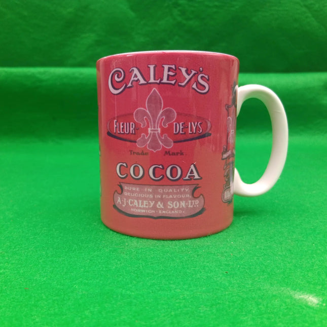 A vintage-style ceramic mug featuring the Caley's Cocoa logo, with a coral-pink body and a white handle, set against a bright green background.