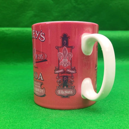 A pink ceramic coffee mug with a white handle, featuring vintage-style printed graphics and text, set against a bright green background.