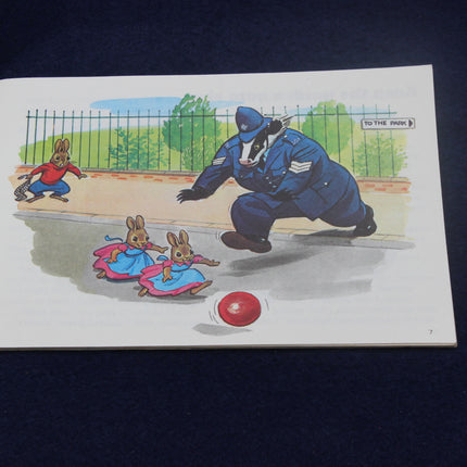 Cartoon illustration of a badger in a police uniform chasing two bunnies with a ball.