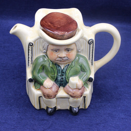 Teapot with a figurine of a man wearing a hat on a blue background