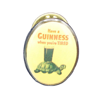 Round yellow enamel badge with Guinness advertisement on a blue textured background