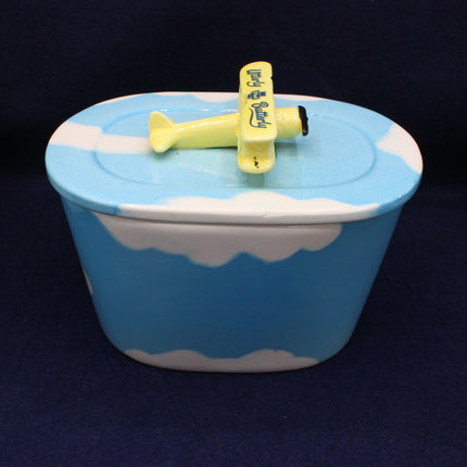 Blue container with white cloud design and yellow airplane on a dark background