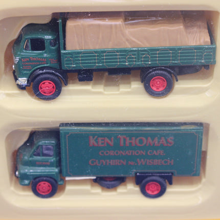 Two model trucks, one with a flatbed and one with a cargo box, in a display case.