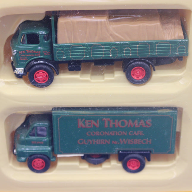 Two model trucks, one with a flatbed and one with a cargo box, in a display case.