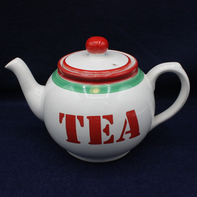 White teapot with red and green accents and 'TEA' text on a dark background