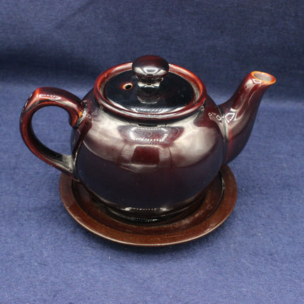 Brown ceramic teapot with lid on a matching saucer against a blue background
