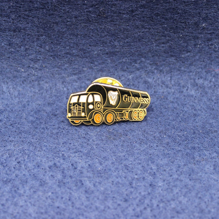 Gold-colored Guiness tanker truck-shaped pin badge on a blue textured background