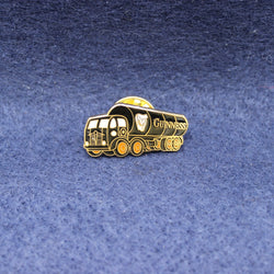 Gold-colored Guiness tanker truck-shaped pin badge on a blue textured background