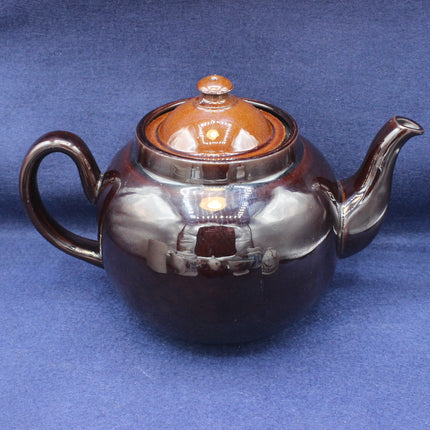 Teapot with a brown ceramic body and silver lid on a blue background