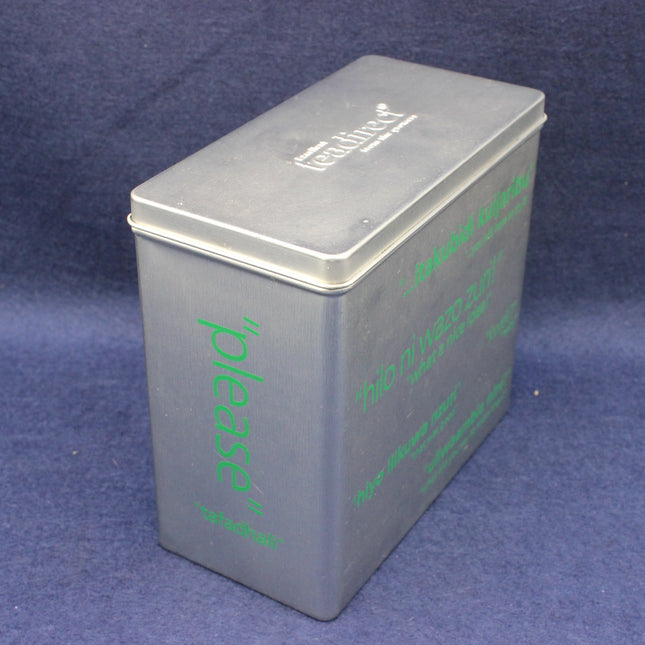 Metallic tea caddy tin with green text on a blue background