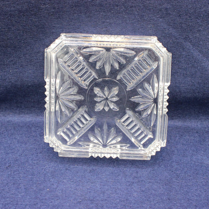 Clear glass decorative ashtray with floral patterns on a blue background