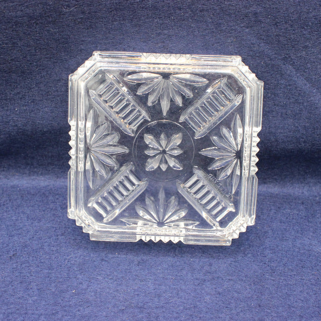 Clear glass decorative ashtray with floral patterns on a blue background