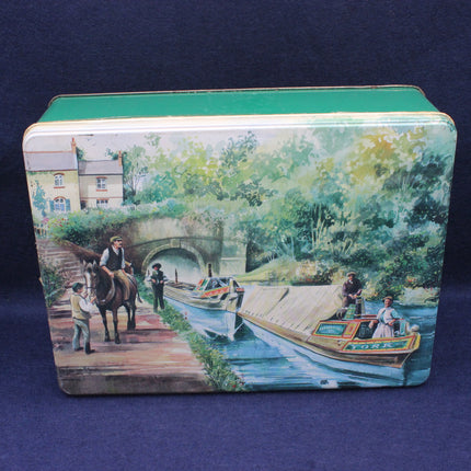 Decorative tin box with a scenic design of a river scene, boat, and people on a blue background.