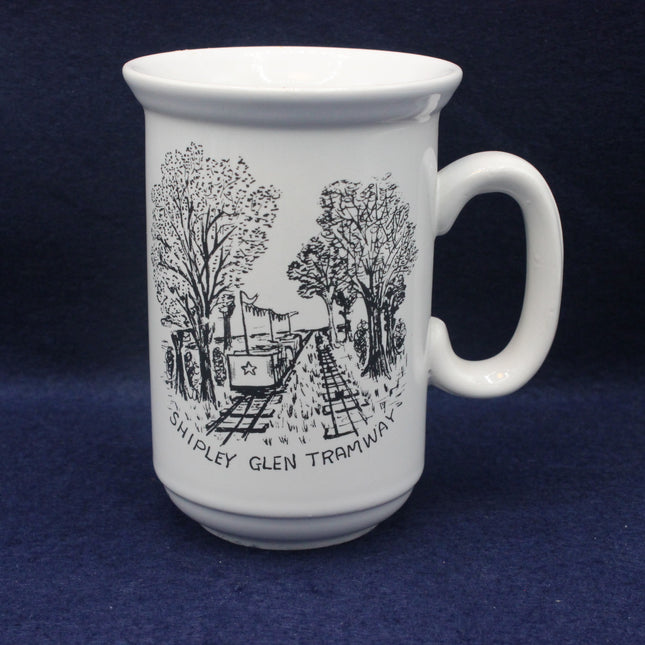 White mug with black illustration of a tram and trees on a blue background