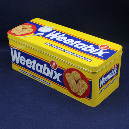 Yellow Weetabix tin with blue and red accents on a dark background