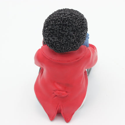A small figurine of a Golly seen from behind, wearing a bright red top and a textured black head covering, with a small blue detail on the side, photographed against a plain white background.