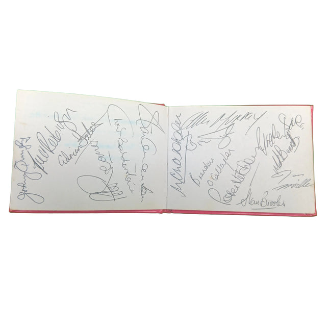 An open book or album with multiple autograph signatures written in black ink on white pages, photographed against a bright green background.