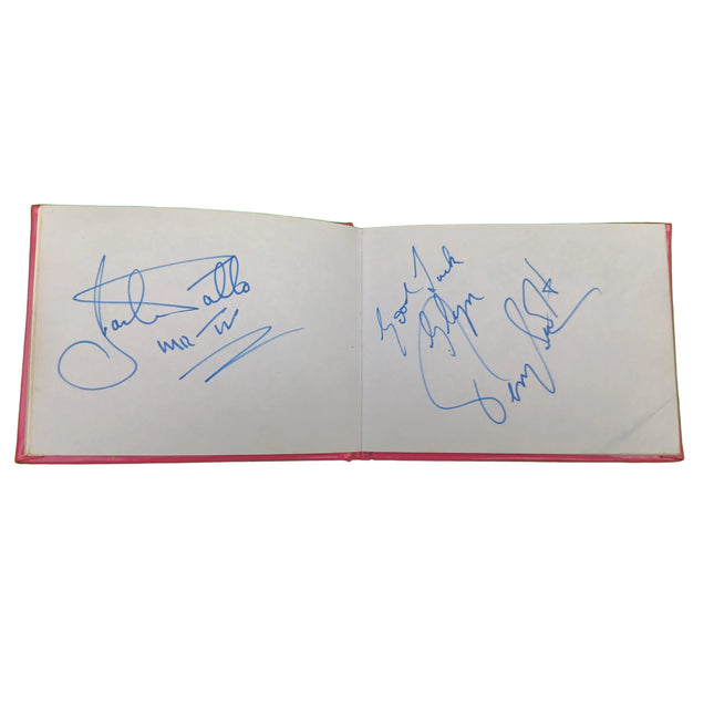 An open book or notebook with blue ink signatures on both white pages, photographed against a bright green background.