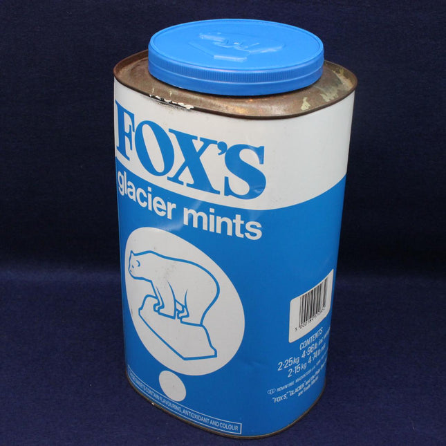 A vintage metal tin of Fox's Glacier Mints with a blue screw-on lid, featuring a blue and white label with a polar bear illustration, set against a dark blue background.