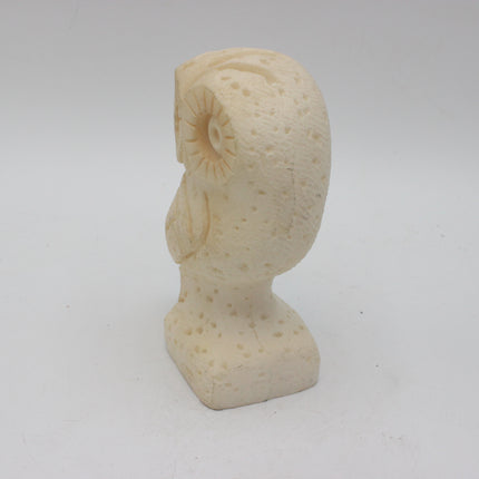 A small carved owl figurine in a light cream or ivory stone-like material, shown standing on a plain light gray background.
