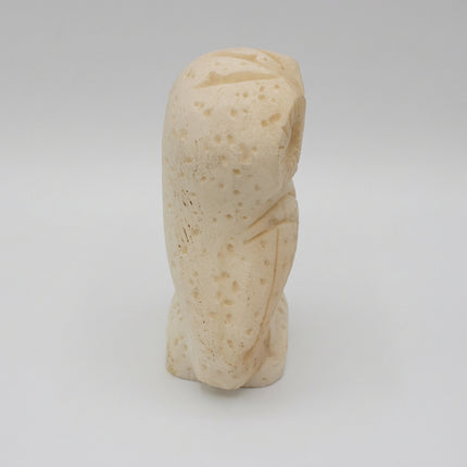 A small carved stone figurine of a seated figure, likely a bust or sculpture, in a light cream or ivory color with a speckled texture, photographed against a neutral light gray background.