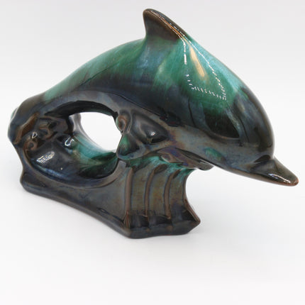 A ceramic dolphin figurine with a glossy, iridescent glaze showing shades of green, teal, and dark blue-black, set against a plain white background.