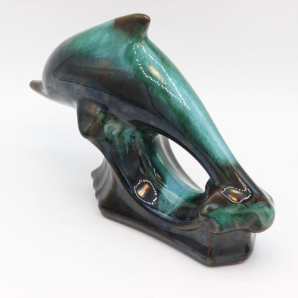 A glossy ceramic dolphin figurine with a vibrant green and dark brown glaze, displayed on a clean white background.