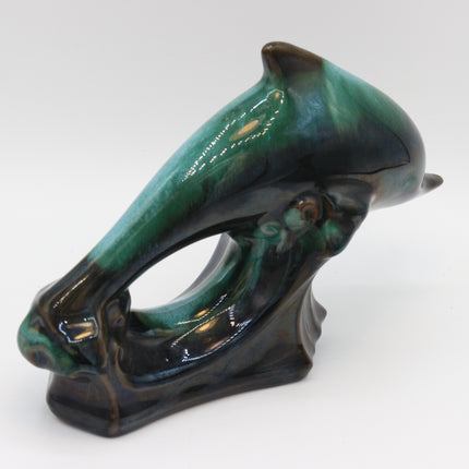 A glossy ceramic dolphin figurine with a green and black glaze, photographed on a neutral light gray background.