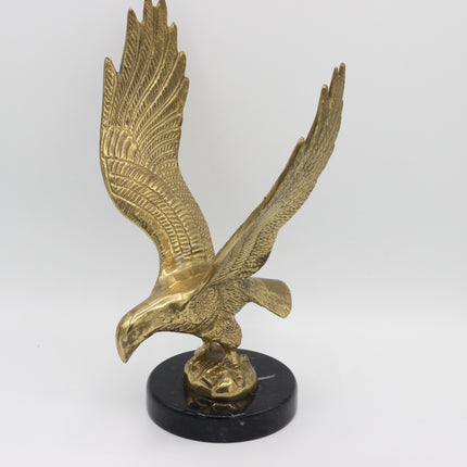A metallic gold eagle sculpture with outstretched wings, mounted on a round black base against a plain light gray background.