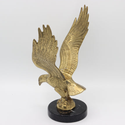 A golden eagle sculpture with wings spread, mounted on a round black marble base, photographed against a neutral light gray background.