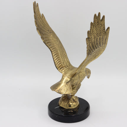 A metallic gold eagle sculpture with wings spread, mounted on a round black base against a light gray studio background.