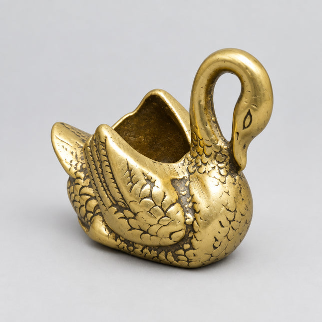 A small metallic swan-shaped container or holder with an open top, photographed on a bright green background.