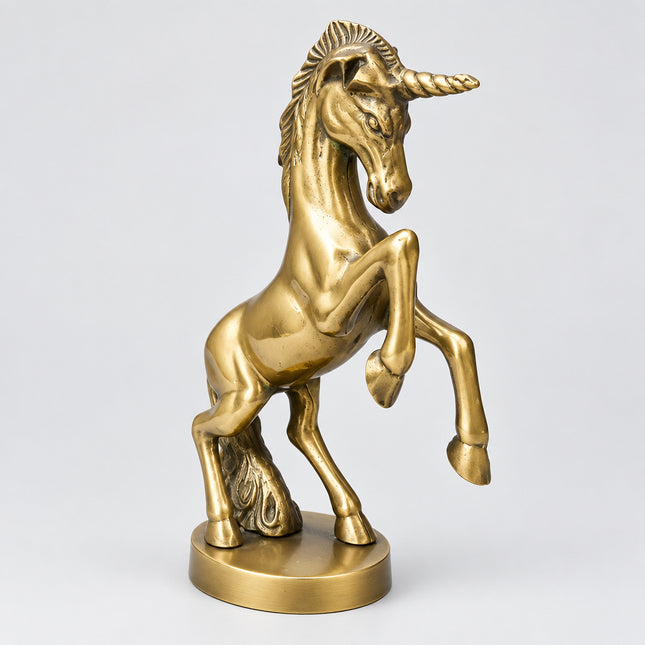 A bronze-finished unicorn figurine standing on a round base, photographed against a green fabric backdrop.