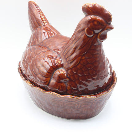 A glossy brown ceramic chicken-shaped container or figurine sitting in a matching basket-like base, photographed on a plain white background.
