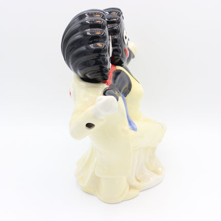 A ceramic figurine of two Gollies, one with a large black helmet-like headpiece and the other in a cream dress, on a plain white background.