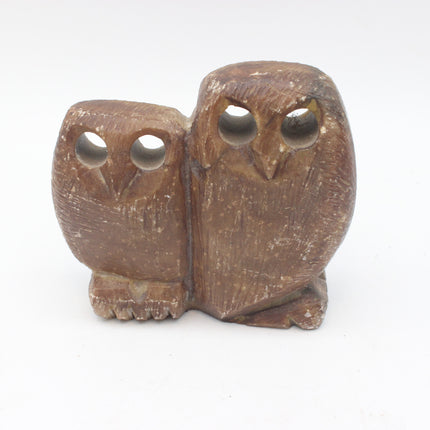 A small carved stone owl figurine with two owls side by side, featuring cut-out eyes and a natural brown wood texture, set against a plain white background.
