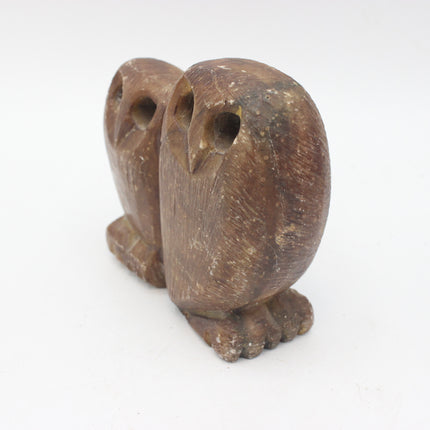 A small carved stone owl figurine in a natural medium-brown wood tone, photographed on a plain white background.