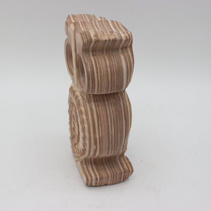 A carved wooden owl figurine with detailed wood-grain stripes in shades of brown, beige, and cream, standing upright on a light gray background.