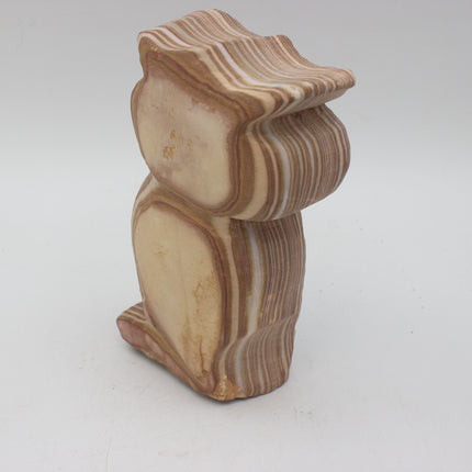 A carved stone owl figurine with natural banded patterns in beige, cream, and brown, photographed on a light gray background.