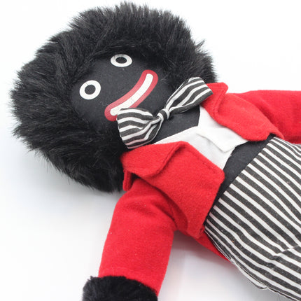 A plush Golly doll with black hair, a black face, a red jacket, a white shirt, a black-and-white striped bow tie, and black-and-white striped pants, photographed on a white background.