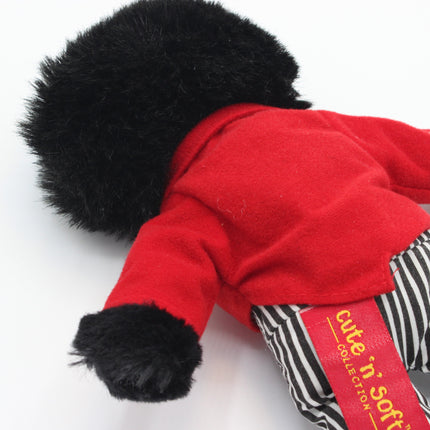 A close-up of a plush Golly toy or doll wearing a bright red jacket with black faux-fur trim at the hood and cuffs, paired with black-and-white striped pants. A red fabric label reads 'cute 'n soft' and 'cute collection', photographed on a plain white background.