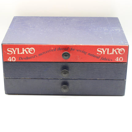 A vintage Sylko sewing thread box with three drawers, featuring a dark blue-gray wooden body and a red top label with white text.