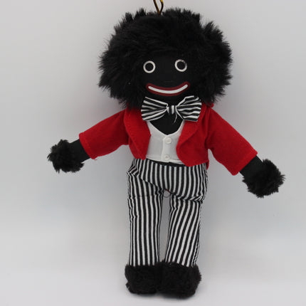 A novelty black-and-white Golly doll with a black fuzzy wig, red jacket, white shirt, black-and-white striped bow tie and trousers, and black fuzzy shoes, photographed against a plain light gray background.