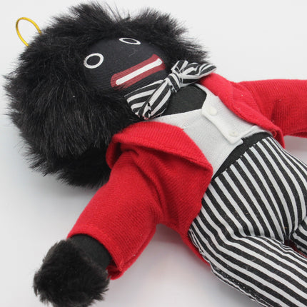 A handmade plush Golly doll with black hair, a black face, a red jacket, a white vest, black and white striped pants, and a black and white striped bow tie, lying on a white background.
