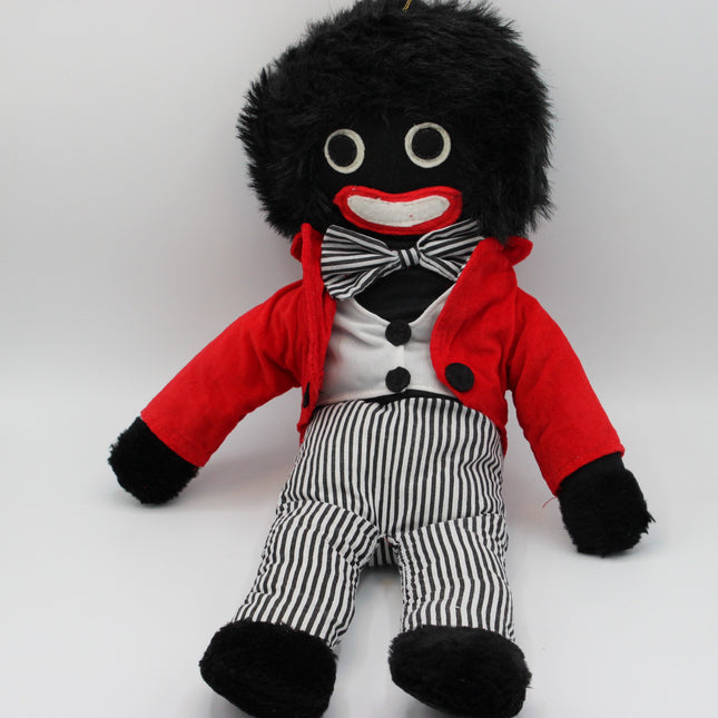 A plush Golly doll with black fuzzy hair, a red jacket, a black-and-white striped shirt and bow tie, and black-and-white striped pants, photographed against a plain light background.