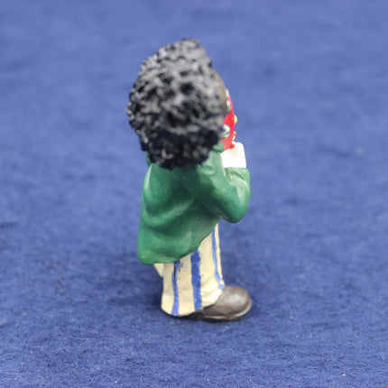 Small figurine of a person in a green jacket and striped pants on a blue background