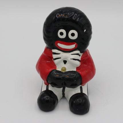 A glossy black and white Golly money box with a red jacket and white pants, shown against a plain light gray background.