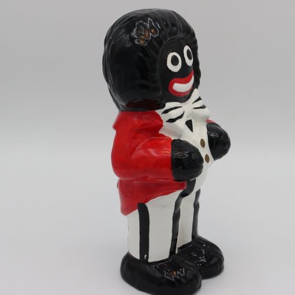 A glossy ceramic figurine of a Golly character with black hair, white face details, a red jacket, and a white-and-black striped outfit, shown against a plain light gray background.