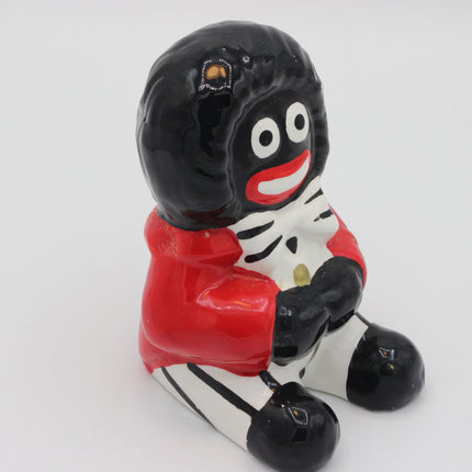 A glossy ceramic figurine of a Golly character with black hair, a red top, and a white-and-black striped lower body, shown against a plain light gray background.