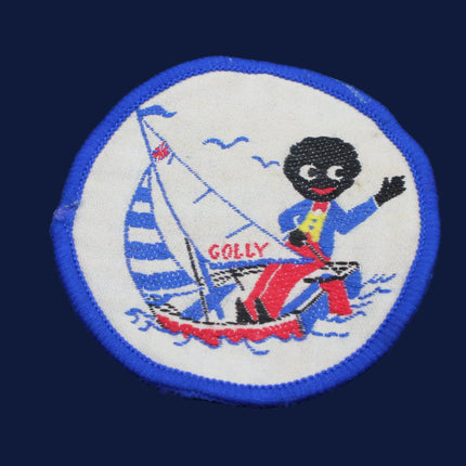 Embroidered patch with a golliwog character on a sailboat, set against a dark fabric background.